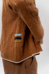 Saco tejido de lambswool color marrón, con diseño inspirado en kimono, mangas largas y delicados calados en toda la prenda. Cuenta con bordes en contraste.