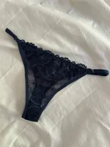 Bombacha tipo colaless de encaje negro con diseño floral, laterales regulables y terminaciones con puntilla.