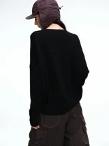 Sweater de punto color negro, con cuello redondo, hombros caídos y terminaciones acanaladas en puños y ruedo. Presenta un diseño de calce relajado y tejido suave.