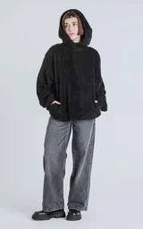 Hoodie oversize tipo anorak confeccionado en piel sintética de corderito, color negro. Presenta cierre central parcial, capucha ajustable con cordones y bolsillo canguro frontal.