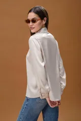 Camisa de seda color crema con cuello clásico, cierre frontal de botones y mangas largas con puños abotonados.