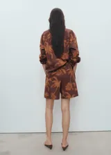 Short de tiro alto con diseño recto, confeccionado en algodón con estampado de palmeras. Presenta detalle de pinzas frontales, trabillas para cinturón, cierre de gancho y cremallera, y dos bolsillos laterales.