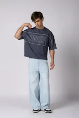 Remera gris oscuro de corte boxy, con mangas cortas y cuello redondo. Cuenta con un diseño gráfico frontal con líneas blancas y la palabra 'CONCEPT' estampada.