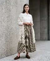 Ruana triangular tejida en telar, de color crudo, con textura de punto abierto y terminaciones con flecos largos en los bordes.