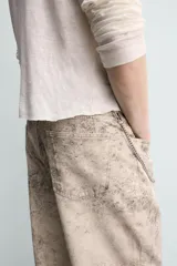 Pantalón de corte baggy fit confeccionado en tejido de algodón con efecto lavado y estampado abstracto en tonos beige y gris. Presenta diseño de cinco bolsillos, cierre frontal con cremallera y botón.