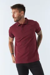 Polo de piqué color bordó, manga corta, con cuello y puños de rib con doble línea negra. Presenta un pequeño logo bordado en el pecho.