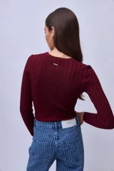 Top de punto ajustado al cuerpo, color bordó, con cuello redondo y mangas largas. Presenta un diseño acanalado vertical con costuras decorativas que forman una silueta en el frente.
