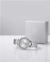 Reloj analógico de pulsera con caja redonda de metal plateado, bisel decorado con cristales y malla de eslabones metálicos. Cuenta con movimiento de cuarzo japonés y cierre desplegable con botón de seguridad.