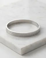 Esclava rígida de acero con acabado plateado y textura grabada con patrón geométrico.