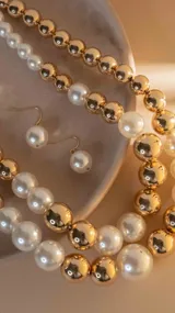 Collar de doble vuelta con cuentas combinadas de perlas blancas y esferas doradas. Incluye aros colgantes con perlas blancas.