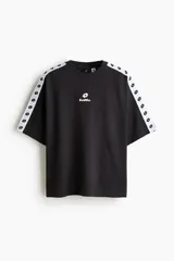 Remera negra de algodón pesado con corte oversized, cuello redondo acanalado, mangas raglán cortas con franja blanca decorativa con el logo de Lotto y logo impreso en el pecho.