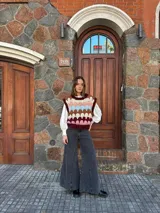 Chaleco tejido de punto con diseño multicolor en bloques, cuello redondo y terminaciones acanaladas. Presenta un patrón geométrico en tonos bordó, rosa, celeste, marrón y crema.