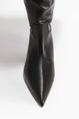 Bota de caña alta hasta la rodilla, confeccionada en material sintético con acabado liso, punta fina y taco kitten. Presenta un diseño con borde superior doblado hacia afuera en sherpa color crema y forro interior de tejido suave para mayor calidez.