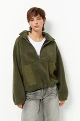 Buzo de textura tipo teddy color verde oliva, con cuello alto y cierre frontal parcial. Presenta bolsillos frontales en tela de nylon a tono y cordón de ajuste en el ruedo.