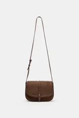 Bolso bandolera de diseño estructurado en color marrón, confeccionado en una combinación de cuero y gamuza. Presenta una solapa frontal con cierre imantado, detalle de tira central con remache metálico y correa larga ajustable para llevar al hombro o cruzado.
