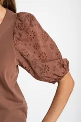 Remera de algodón color rosado con mangas cortas abullonadas de broderie con diseño floral calado. Presenta cuello redondo y costura vertical central en el frente.