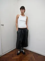 Bermuda de pierna amplia y largo cropped, confeccionada en cuerina negra con acabado levemente brillante. Presenta pretina elástica, pinzas frontales que aportan volumen, bolsillos laterales y un bolsillo ojal en la parte trasera.