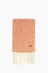 Bufanda de tejido de punto con diseño bicolor, cuerpo en tono naranja y flecos largos en color blanco. Incluye un pequeño parche de cuero sintético con logo en una esquina.