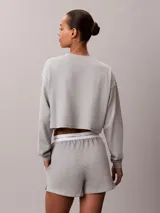 Top cropped de manga larga en tejido de punto de algodón color gris melange. Presenta cuello redondo, hombros caídos y un bolsillo de parche en el pecho con el logo de la marca bordado.