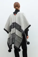 Capa abierta tejida en jacquard color gris y negro con diseño geométrico y detalle de pompones en el borde inferior.