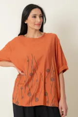 Blusa color ladrillo con estampado de flores y líneas negras, de corte holgado, cuello redondo y mangas cortas con puños elásticos.