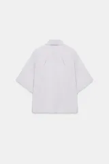 Camisa de manga corta color marrón oscuro, con cuello solapa, corte fluido y cierre frontal oculto con botones.
