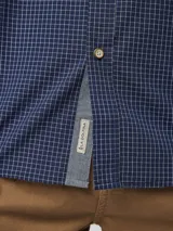 Camisa de manga larga con estampado de cuadros pequeños en tonos azul marino y blanco. Presenta cuello clásico con botones, cierre frontal abotonado y puños ajustables.