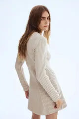 Vestido corto de punto acanalado con diseño entallado, cuello redondo y mangas largas con puños acampanados. Presenta una falda con leve vuelo y detalles de tejido menguado en el frente y la espalda.