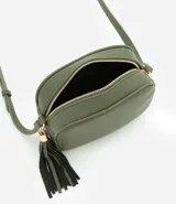 Cartera bandolera pequeña color beige, confeccionada en poliuretano con textura granulada. Presenta cierre superior con cremallera, correa larga ajustable y detalle de borla decorativa en el lateral con herrajes dorados.