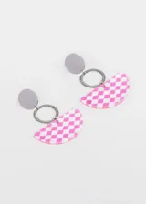 Par de aros colgantes con base de acero quirúrgico, un dije circular plateado, un aro plateado y un dije semicircular de acrílico con estampado a cuadros blancos y negros.