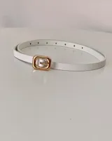 Cinto fino de color blanco con hebilla rectangular metálica en tono dorado.