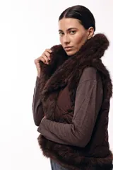 Chaleco acolchado color marrón con terminaciones de piel sintética en los bordes y cuello, aportando volumen y textura.