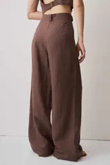 Pantalón de tiro alto color chocolate, con pinzas frontales que aportan caída suave y silueta amplia de pierna recta. Cierra con botón y bragueta, y suma un detalle de botón funcional en la cintura que le da un aire sastrero.