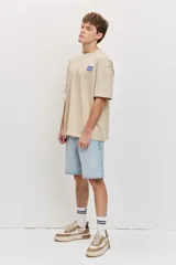 Remera de corte oversize color blanco tiza, de manga corta y cuello redondo, con pequeño estampado gráfico azul en el pecho.