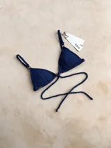Top de bikini triangular color azul marino brillante, con argollas decorativas, bretel decorativo removible, forro y relleno removible. Los breteles son regulables y se ata en la espalda.