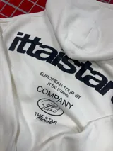 Hoodie de color blanco con capucha, diseño de corte holgado y estampado gráfico en la espalda con tipografía negra.