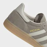 Championes Adidas Handball Spezial de diseño clásico, confeccionados en ante vacuno suave color gris con las icónicas tres tiras laterales en tono más claro. Presentan suela de goma color caramelo y cierre de cordones.