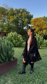 Ruana tejida a mano de lana merino 100%, color negro, con flecos largos en el borde.