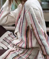 Cárdigan blanco de lana merino tejido en punto jersey, con diseño de rayas verticales bordadas a mano en tonos pasteles en el frente y las mangas. Cuenta con cuello redondo y cierre frontal con botones al tono.