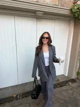 Conjunto de blazer y pantalón de lino gris con diseño de rayas diplomáticas. El blazer es de corte amplio con doble botonadura, y el pantalón es de corte recto y tiro alto.