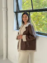 Tapado de estilo aviador en color chocolate con interior y detalles de corderito en color beige. Presenta cierre frontal cruzado con botones, solapas amplias y puños con borde de corderito.