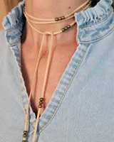 Collar estilo corbatín confeccionado en tiento de cuero, con diseño de múltiples vueltas y detalle de cuentas metálicas en los extremos y a lo largo de la tira.