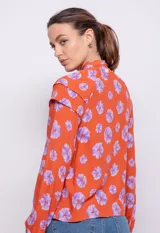 Camisa naranja con estampado de flores lilas, de manga larga con botones de plástico y detalle de alforzas en hombros.