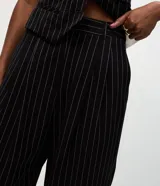Pantalón de sastrería corte carrot, color negro con rayas verticales blancas. Presenta pinzas frontales, cintura con pasantes y bajo ajustado.