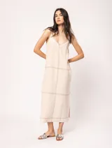 Vestido largo color crudo de lino, con silueta recta, escote en V, breteles anchos, detalle de elástico en la espalda y tajos laterales.