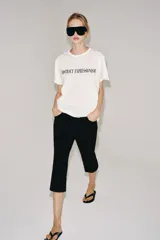 Camiseta oversize blanca de manga corta y cuello redondo, confeccionada en hilatura de algodón con detalle de texto estampado en contraste en el pecho.