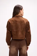 Chaqueta de efecto gamuza en color marrón, con diseño de inspiración western que presenta flecos en la parte frontal y en la espalda. Cuenta con cuello clásico, cierre frontal con botones metálicos a presión y mangas largas.