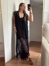 Chaleco largo sin mangas, tejido en punto calado tipo red con hilo de algodón y lurex, color marrón. Presenta escote profundo en V, tiras para atar en el frente, tajo trasero y flecos en el ruedo.