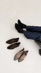 Botinetas de gamuza color marrón oscuro con detalle de flecos en el empeine y correa con tachas metálicas doradas. Poseen suela plana y diseño de caña baja.