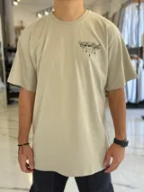 Remera oversize color beige, con mangas corta y gran estampado gráfico en la espalda con texto en negro.